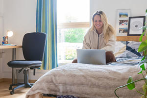 a smiling student is sitting on a bed in Ƶ accommodation